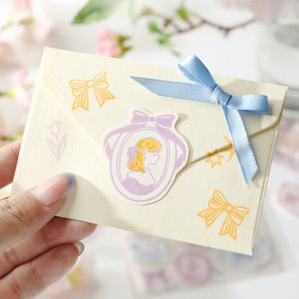 Hand holding a small card with decorative stickers featuring bows and a profiled face on a floral background.