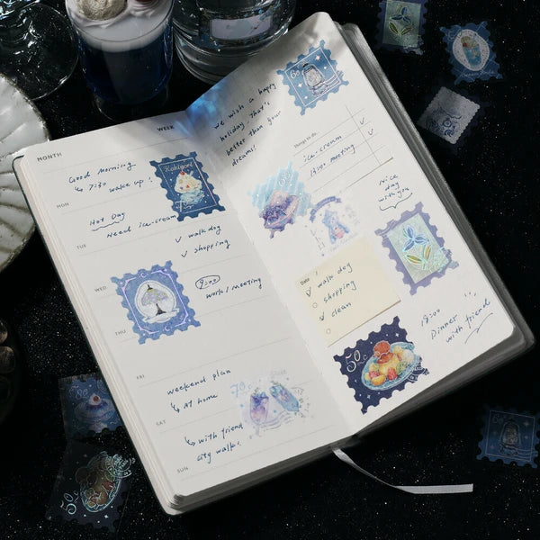 Open notebook with decorative stickers and handwritten text on a dark surface.
