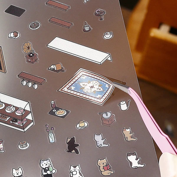 Sticker sheet with various small illustrations including cats, a table, and other objects on a brown background.