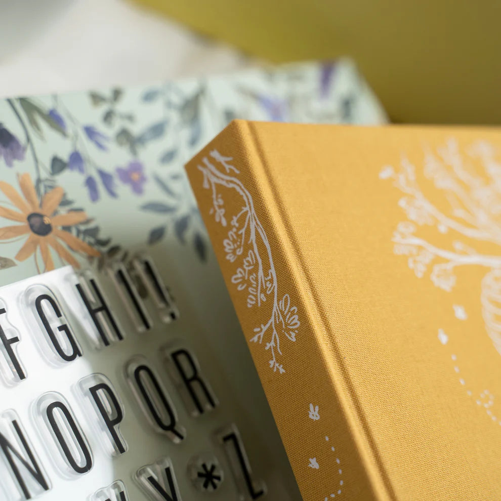 Yellow book with floral design on a surface with a white letter board. June Quarterly Box Beekeeper’s Garden from Archer & Olive.