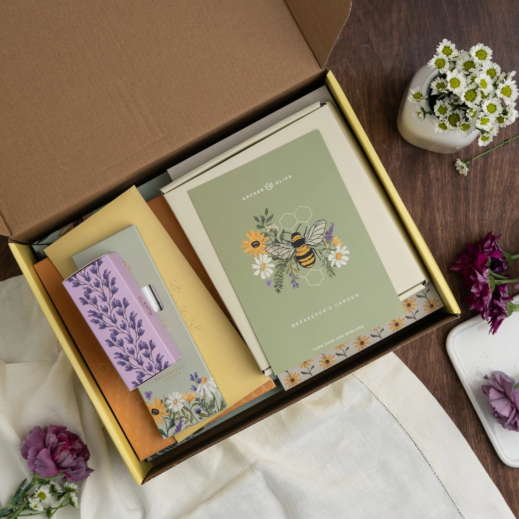 Open box containing stationery items with a floral design on a wooden surface. June Quarterly Box Beekeeper’s Garden from Archer & Olive.