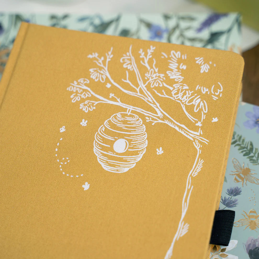 Yellow notebook with white tree and beehive design on a floral background. June Quarterly Box Beekeeper’s Garden from Archer & Olive.
